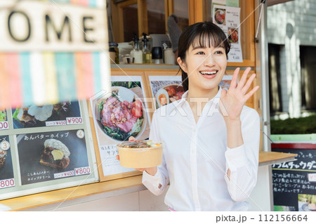 キッチンカーの前でお客に呼びかける女性 キッチンカーの前でお客に呼びかける女性 112156664