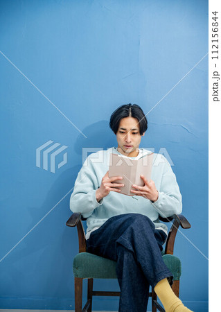 ブルーバックで椅子に座り本を読む若い男性 ブルーバックで椅子に座り本を読む若い男性 112156844