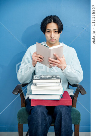 ブルーバックで椅子に座り本を読む若い男性 112156857