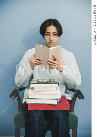ブルーバックで椅子に座り本を読む若い男性 ブルーバックで椅子に座り本を読む若い男性 112156858
