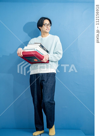 ブルーバックで本を持ちながら立つ若い男性 ブルーバックで本を持ちながら立つ若い男性 112156918