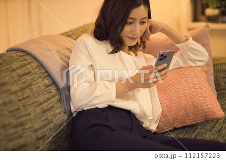 ジャケットを脱いでソファでスマホを見るビジネスウーマン のナイトルーティーン　 112157223