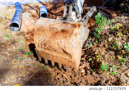 An excavator digs trench for laying pipe through which rainwater will flow to collector 112157939