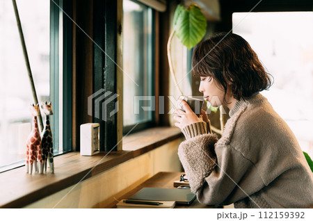 カウンターで温かい飲み物を飲む笑顔の女性 カウンターで温かい飲み物を飲む笑顔の女性 112159392