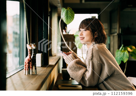 窓際のカウンターでスマホを使う笑顔の女性 112159396