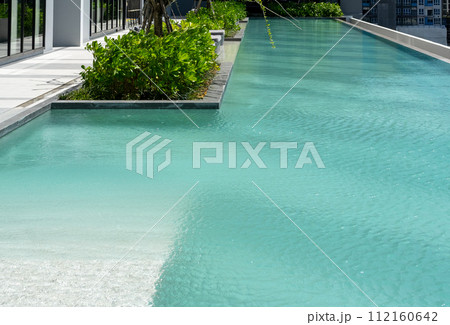Elegant infinity pool with crystal clear water against a backdrop of city buildings and lush foliage.Infinity Pool Overlooking Urban Landscape.. 112160642