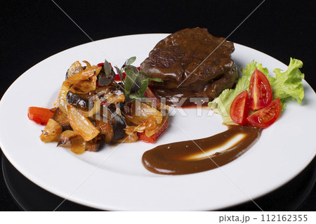 On a white plate fried meat with gravy, stewed vegetables, lettuce leaves, sauce, basil and tomato cut.Beef in sauce. On a white plate fried meat with gravy, stewed vegetables, lettuce leaves, sauce, basil and tomato cut.Beef in sauce. 112162355