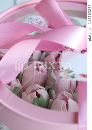 Zephyr in a box. Marshmallow tulips. The box is pink, tied with a ribbon. It stands on white boards. Taken from above. Close-up. Zephyr in a box. Marshmallow tulips. The box is pink, tied with a ribbon. It stands on white boards. Taken from above. Close-up. 112163242
