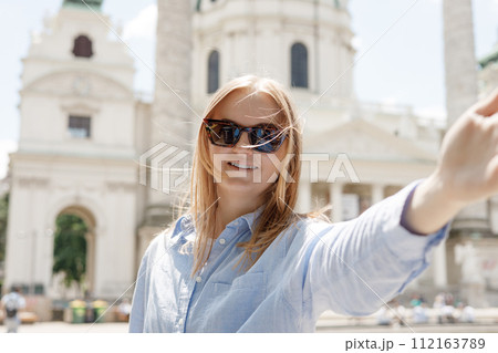 Photo relaxed charming positive young woman hold camera and make selfie summer outside in city center outdoors. Lifestyle tourist travel holiday concept. Point of view. St. Charles's Church, Vienna Photo relaxed charming positive young woman hold camera and make selfie summer outside in city center outdoors. Lifestyle tourist travel holiday concept. Point of view. St. Charles's Church, Vienna 112163789
