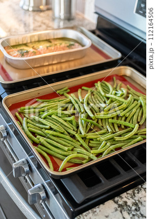 Watch as fresh green beans are beautifully roasted to perfection on a baking sheet with a silicone mat, adding a burst of flavor to your meal. 112164506