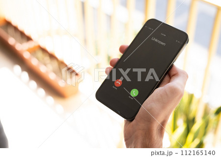 Fraud or fraudulent schemes. Close-up of a male hand holding a phone with an unexpected incoming call from an unknown 112165140