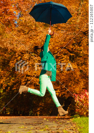 Woman jumping with umbrella in park during autumn 112165807