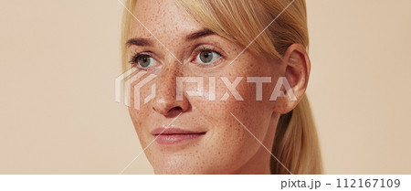 Cropped portrait of young blond woman with freckles. Female with smooth healthy skin against a pastel backdrop. Cropped portrait of young blond woman with freckles. Female with smooth healthy skin against a pastel backdrop. 112167109