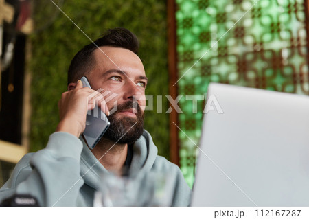 Cheerful young adult man in casual clothes in cafe talking on a mobile phone 112167287