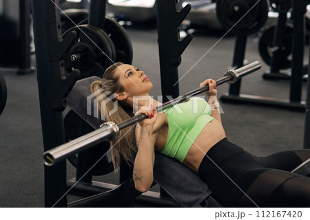 Young fit slim woman in sportswear trains pectoral muscles doing incline chest press in the gym. Young fit slim woman in sportswear trains pectoral muscles doing incline chest press in the gym. 112167420