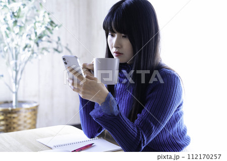 勉強中にスマホとコーヒーで休憩する女性 112170257