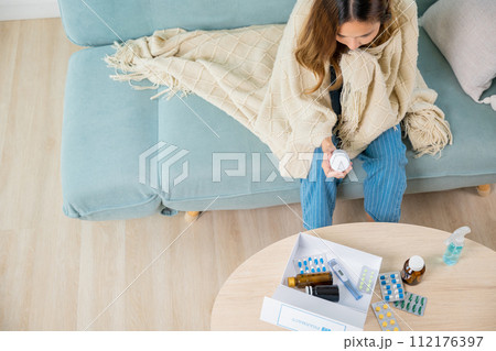 Asian young woman reading ingredient and hold bottle of drug on sofa at home, sick people reading information medicine label pills, female with flu virus, Health care and medicine concept 112176397