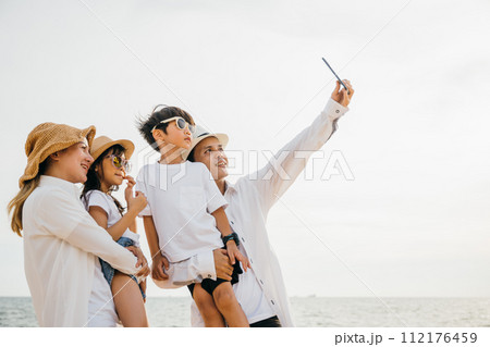 A happy family cherishing moments on the beach capturing laughter and joy while taking a delightful selfie near the sea. A heartwarming portrayal of togetherness during a summer vacation. 112176459