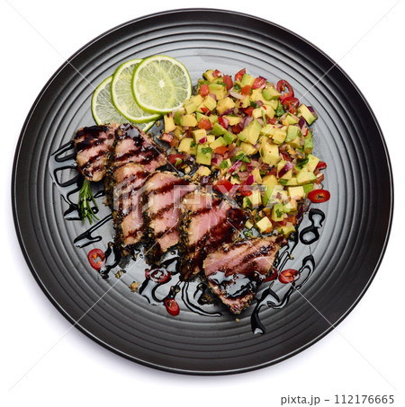 Sliced Organic grilled Tuna fillet covered with sesame seeds and salsa on black ceramic plate 112176665