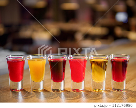 Set of colorful different bitters and liqueurs in shot glasses on bar counter. Collection of shooters. Selection of natural berry alcoholic tinctures in glasses. Different bitters and liqueurs Set of colorful different bitters and liqueurs in shot glasses on bar counter. Collection of shooters. Selection of natural berry alcoholic tinctures in glasses. Different bitters and liqueurs 112176980