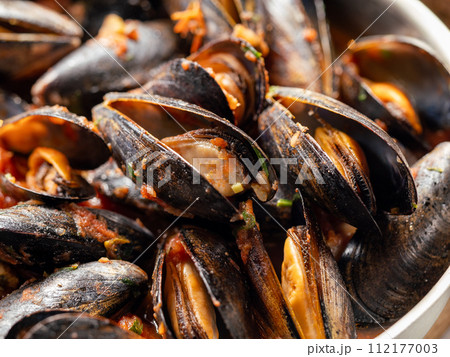 Delicious black mussels in red tomato sauce close up. Mediterranean black mussels in metal pan. 112177003