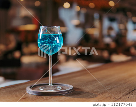 Glass of blue lagoon cocktail in shark high stem cocktail glass on beautiful bar counter background with copyspace. Aesthetic photo of blue lagoon cocktail in evening light, restaurant or bar interior Glass of blue lagoon cocktail in shark high stem cocktail glass on beautiful bar counter background with copyspace. Aesthetic photo of blue lagoon cocktail in evening light, restaurant or bar interior 112177045