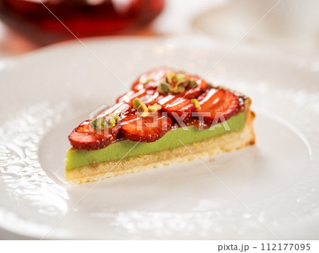 Pistachio cake decorated with strawberries. Crispy tart crust with Pistachio filled layer, decorated fresh strawberry. Portion of perfect pistachio tart on restaurant table 112177095