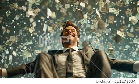 Jackpot winner sits in a chair with a big smile under a rain of money, reveling in his newfound wealth. 112178634