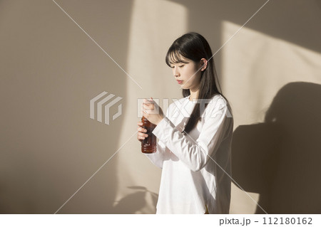 室内でペットボトルのお茶を開ける若い女性 112180162