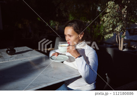 Portrait of a beautiful woman drinking freshly brewed coffee in outdoor cafe, enjoying breakfast before going to work 112180886