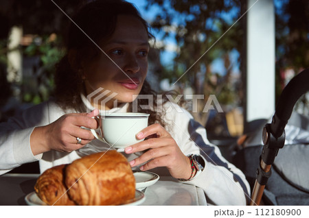 Beautiful woman takes her breakfast in the street cafe, drinks freshly brewed espresso coffee and eats crispy croissants 112180900