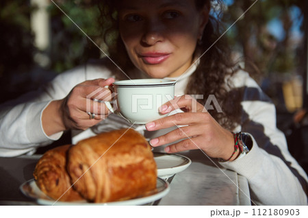 Pretty woman sipping espresso coffee, enjoying slow life with morning vibe at city square with sweet crispy croissants 112180903