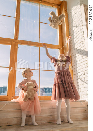 two cute little sisters with bear toys playing near window two cute little sisters with bear toys playing near window 112182096