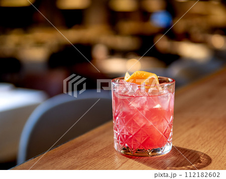 Transparent pink alcohol cocktail with ice, aperol and gin on bar counter in restaurant interior. Alcohol cocktail decorated orange zest spiral. Cold alcoholic cocktail in bar or nightclub. Copy space 112182602