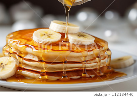 Stack of pancakes with maple syrup and banana slices on top. 112184440