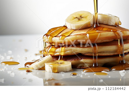Stack of pancakes with maple syrup and banana slices on top. 112184442