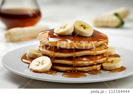 Stack of pancakes with maple syrup and banana slices on top. 112184444