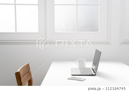 窓際の白いテーブルの上のノートパソコンとスマホとマグカップ 112184745