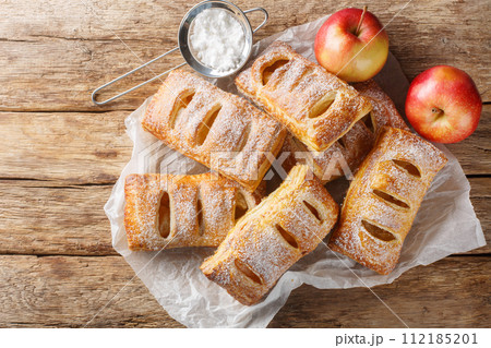 Freshly baked apple puff pastries with powdered sugar close-up on a paper. Horizontal top view Freshly baked apple puff pastries with powdered sugar close-up on a paper. Horizontal top view 112185201