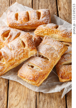 Danish apple puff pastry covered with powdered sugar close-up. Vertical Danish apple puff pastry covered with powdered sugar close-up. Vertical 112185213
