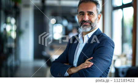 Portrait of a successful  businessman with confident and friendly facial expression and his arms crossed in front of blurred office background. Generative AI 112185422