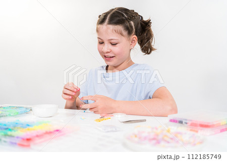 Little girl enjoys crafting colorful bracelets with vibrant clay beads set. Little girl enjoys crafting colorful bracelets with vibrant clay beads set. 112185749