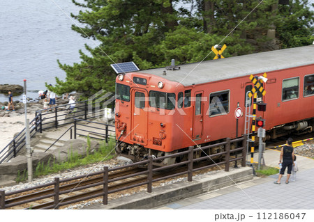 雨晴海岸の義経岩脇の踏切を通る氷見線のタラコ列車 雨晴海岸の義経岩脇の踏切を通る氷見線のタラコ列車 112186047
