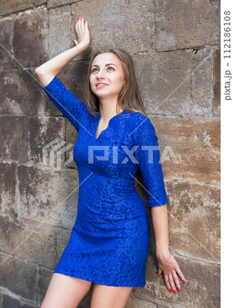 Elegant girl is posing in blue dress near old wall 112186108