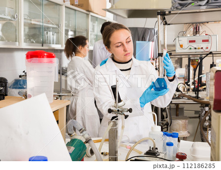 Female chemist analyzing liquid in test flasks Female chemist analyzing liquid in test flasks 112186285