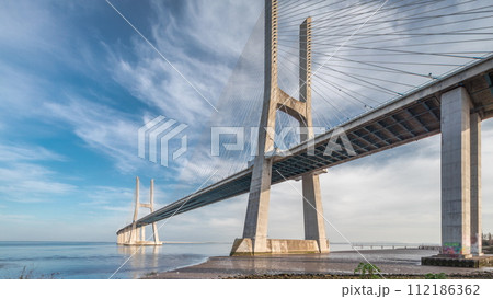 Vasco da Gama bridge timelapse hyperlapse with water in river and blue cloudy sky. Lisbon, Portugal. 112186362