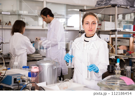 Female chemist analyzing liquid in test flasks Female chemist analyzing liquid in test flasks 112186454