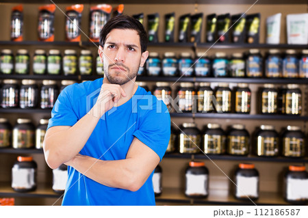 muscular man standing near shelves with sport nutrition muscular man standing near shelves with sport nutrition 112186587