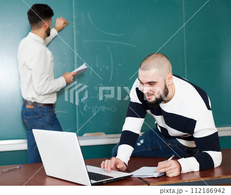 Students working with laptop near blackboard 112186942