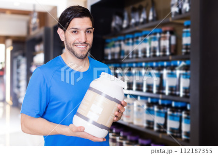 Smiling athletic man seller holding sport nutrition products Smiling athletic man seller holding sport nutrition products 112187355